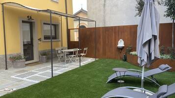 A courtyard with artificial grass, a covered seating area, and a dining table with chairs.