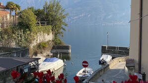 A coastal view with mountains in the background, a dock with boats, and a building with a balcony overlooking the water. - Al Molo 5 Apartments (Oliveto Lario)