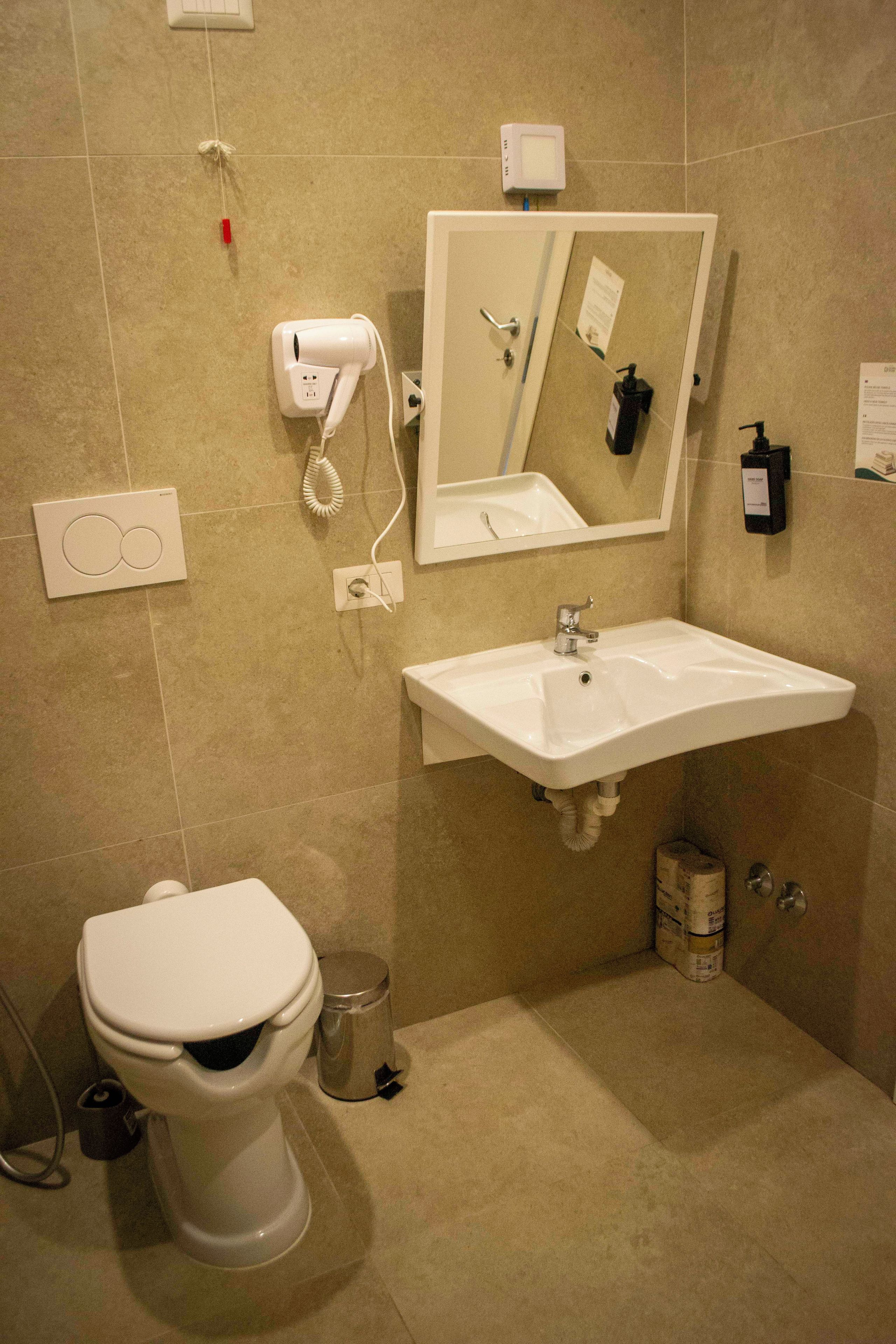 A bathroom with a toilet, sink, mirror, and hairdryer on the wall.