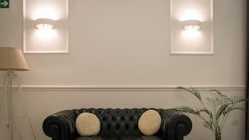 Un canapé en cuir noir avec deux coussins, une lampe et une plante en pot, le tout placé contre un mur orné de deux appliques murales éclairées.