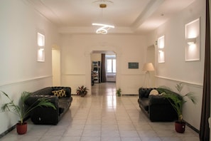 Eine Hotelhalle mit einem zentralen Korridor, zwei Sofas mit Blumentöpfen, einer Kaffeemaschine und einer Lampe.