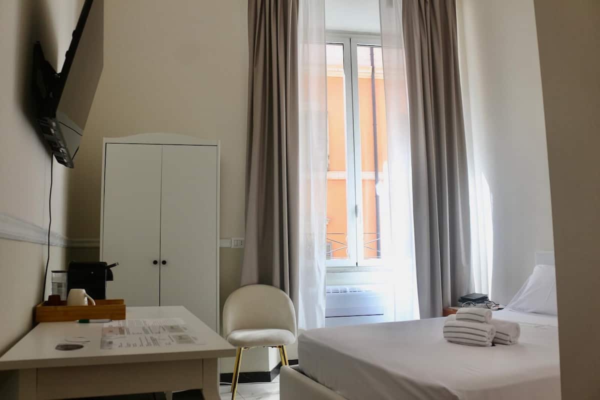 A hotel room with a bed, a desk, a chair, a wardrobe, and a window with curtains.