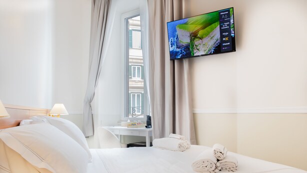 A hotel room with a bed, a desk, a TV, and a window with curtains. - Hotel Domus Rome (Rome)