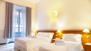 A hotel room with two beds, a large window with curtains, and wall-mounted lamps. - Hotel Domus Rome (Rome)
