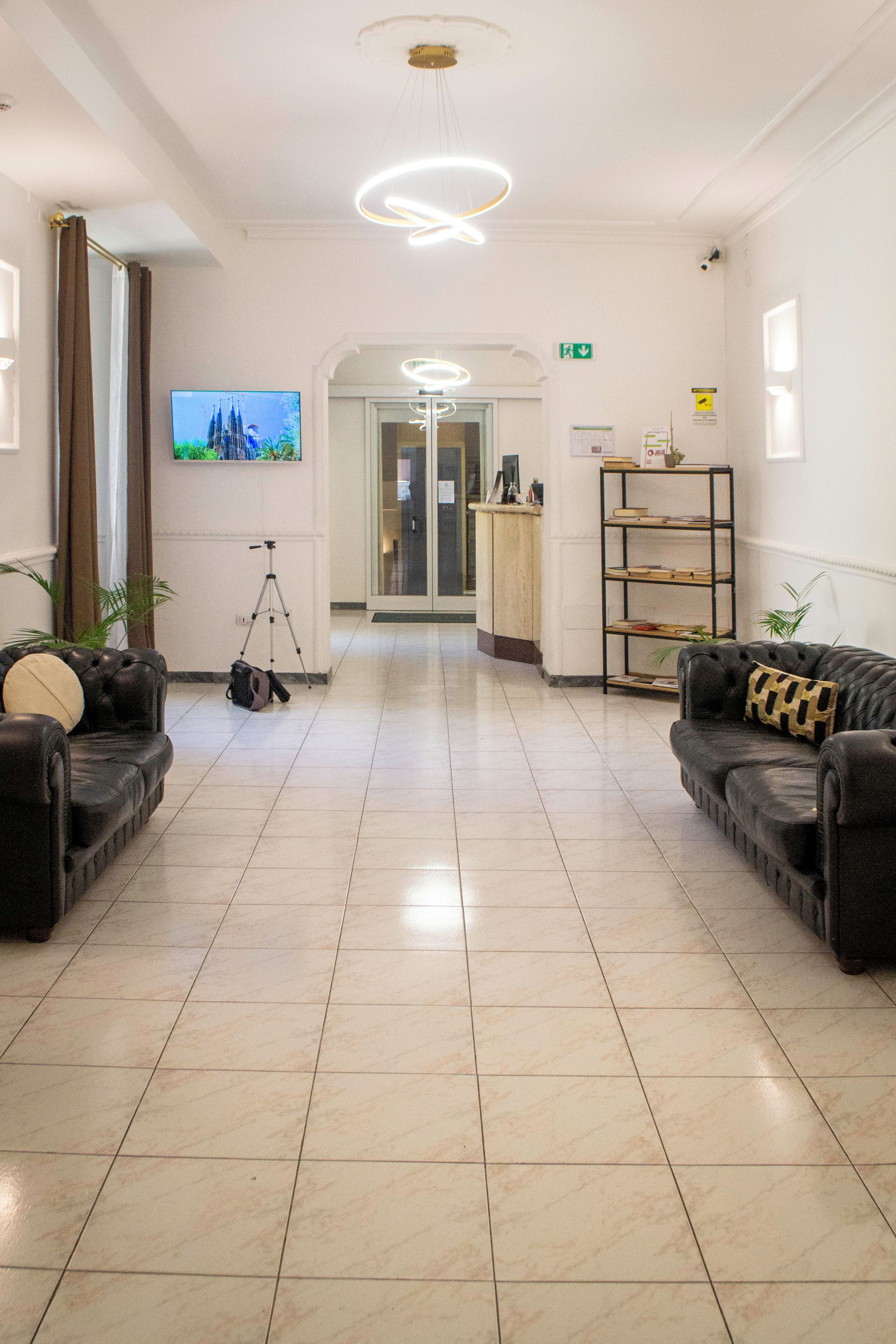 Un hall de hotel con un mostrador de recepción, dos sofás, un trípode y un televisor en la pared.