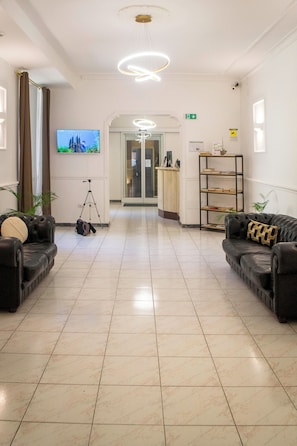 Eine Hotelhalle mit einer Rezeption, zwei Sofas, einem Stativ und einem Fernseher an der Wand.
