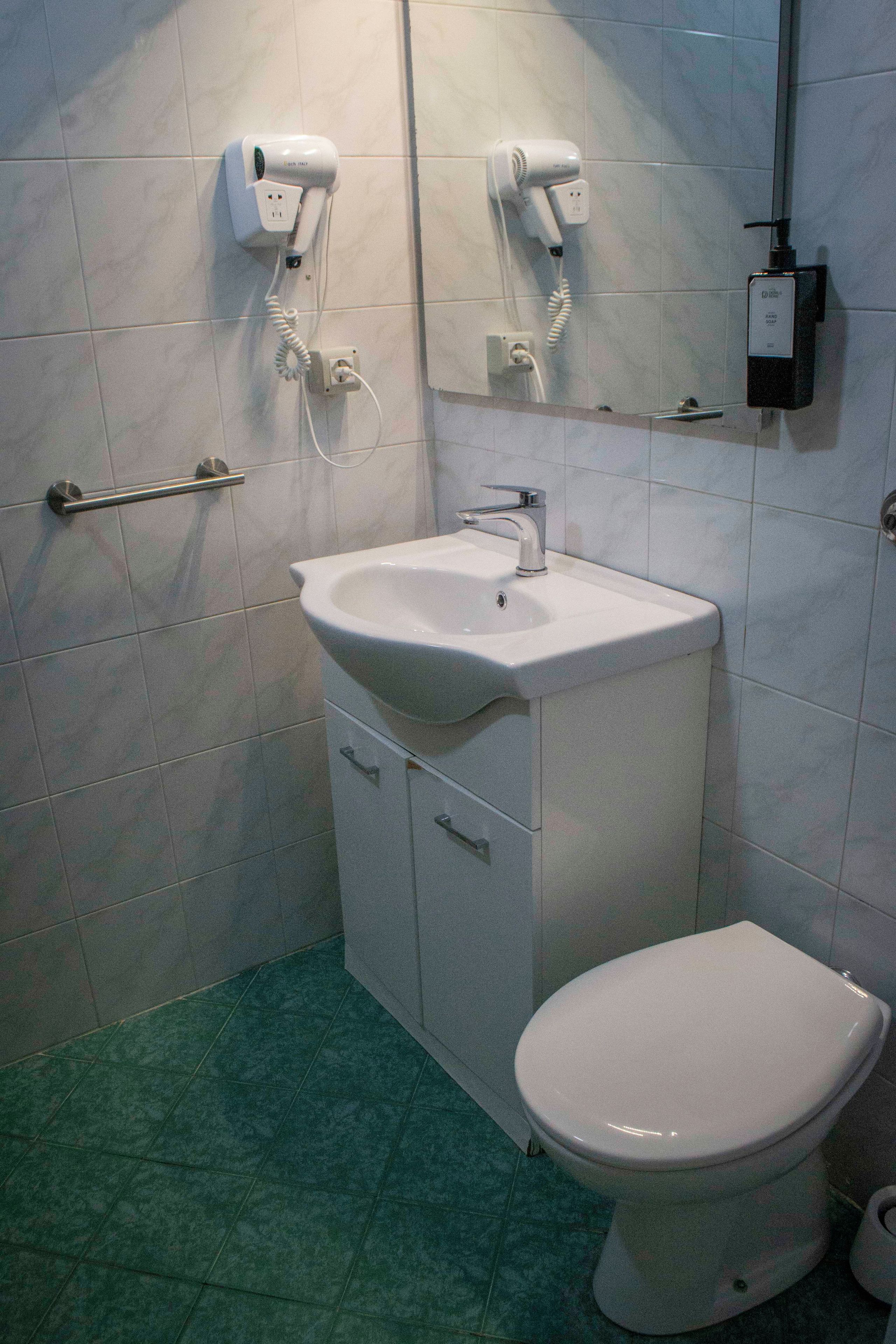 A bathroom with a white sink, a toilet, and two hair dryers mounted on the wall.