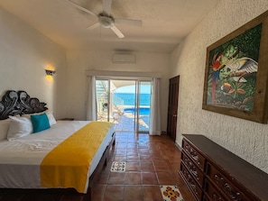 A hotel room with a bed, a dresser, a painting, and a view of the ocean.