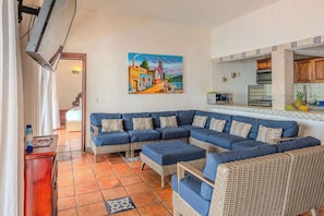 A living room with a large sectional sofa, a kitchen with a tiled backsplash, and a painting on the wall.