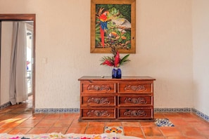 Un aparador de madera con detalles tallados, un cuadro enmarcado de pájaros y un florero con flores encima.