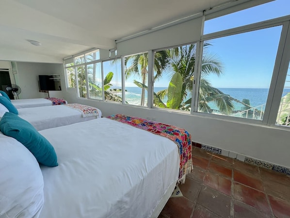 Habitación de hotel con dos camas, un ventanal con vista al océano y piso de baldosas.