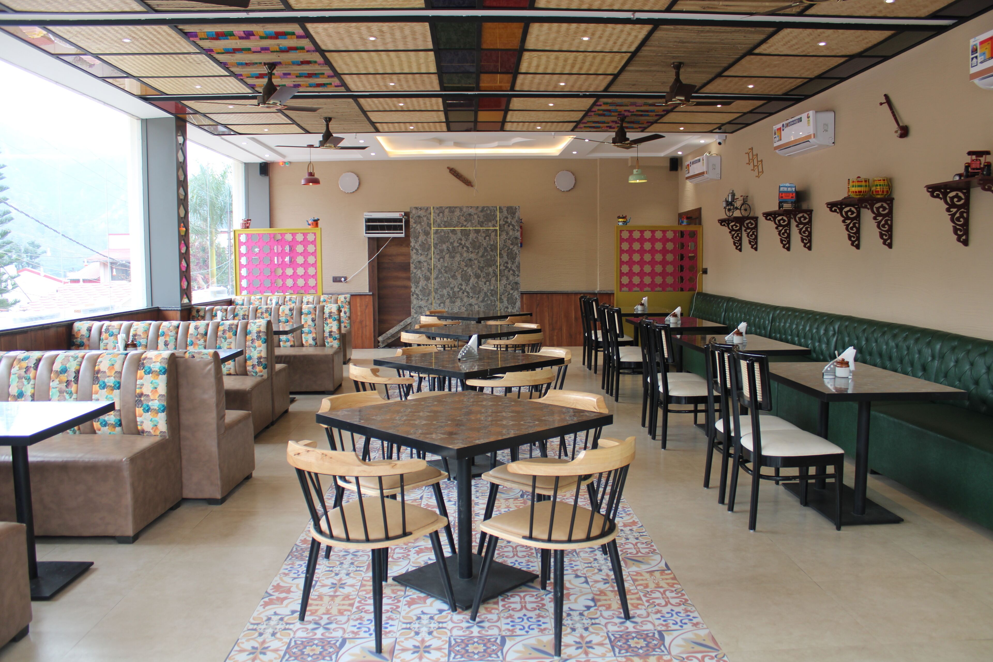 Interior de restaurante con cabinas, mesas redondas y sillas. Se observan ventiladores de techo, adornos en las paredes y un piso con diseño.