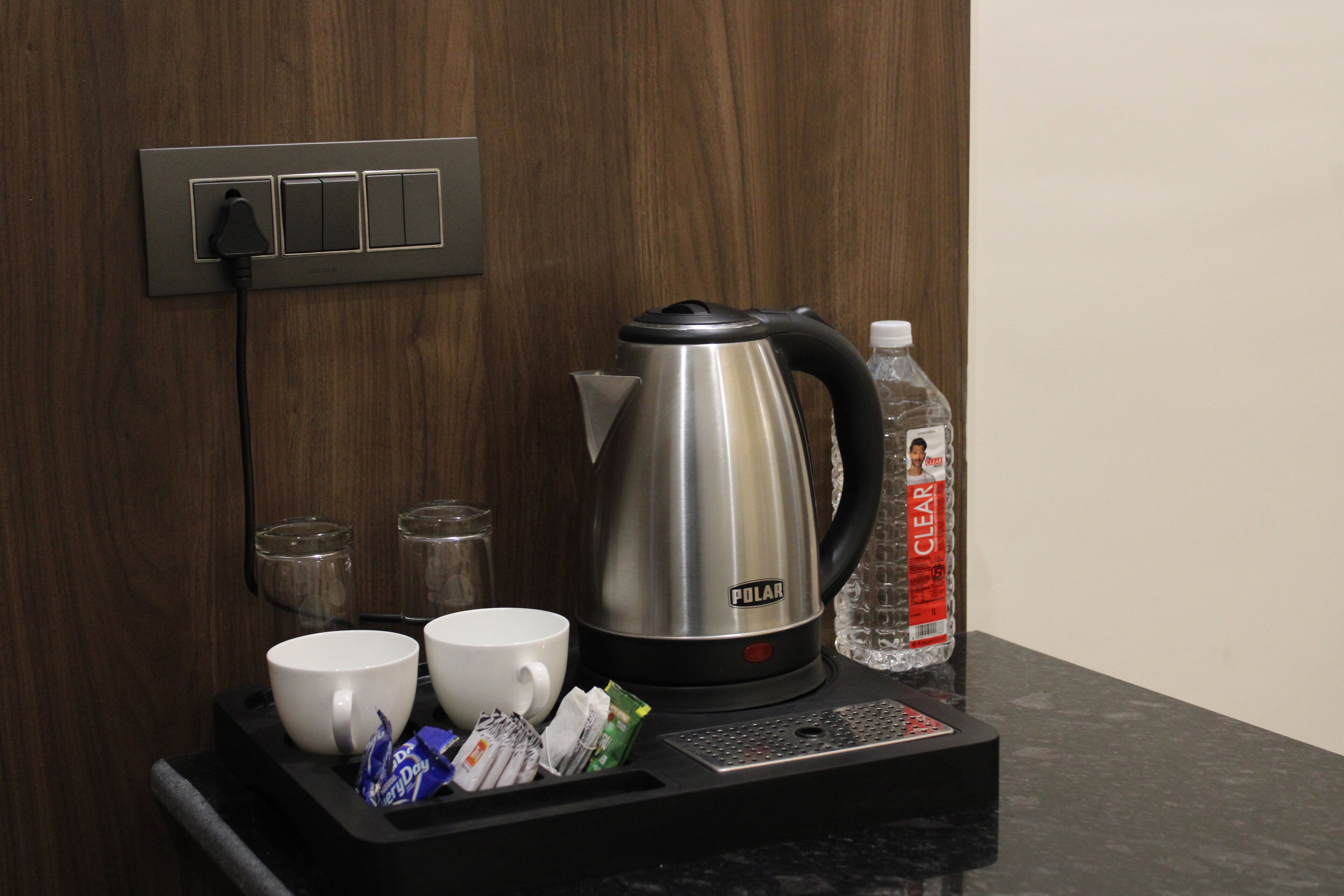 A coffee station with a kettle, cups, and condiments.