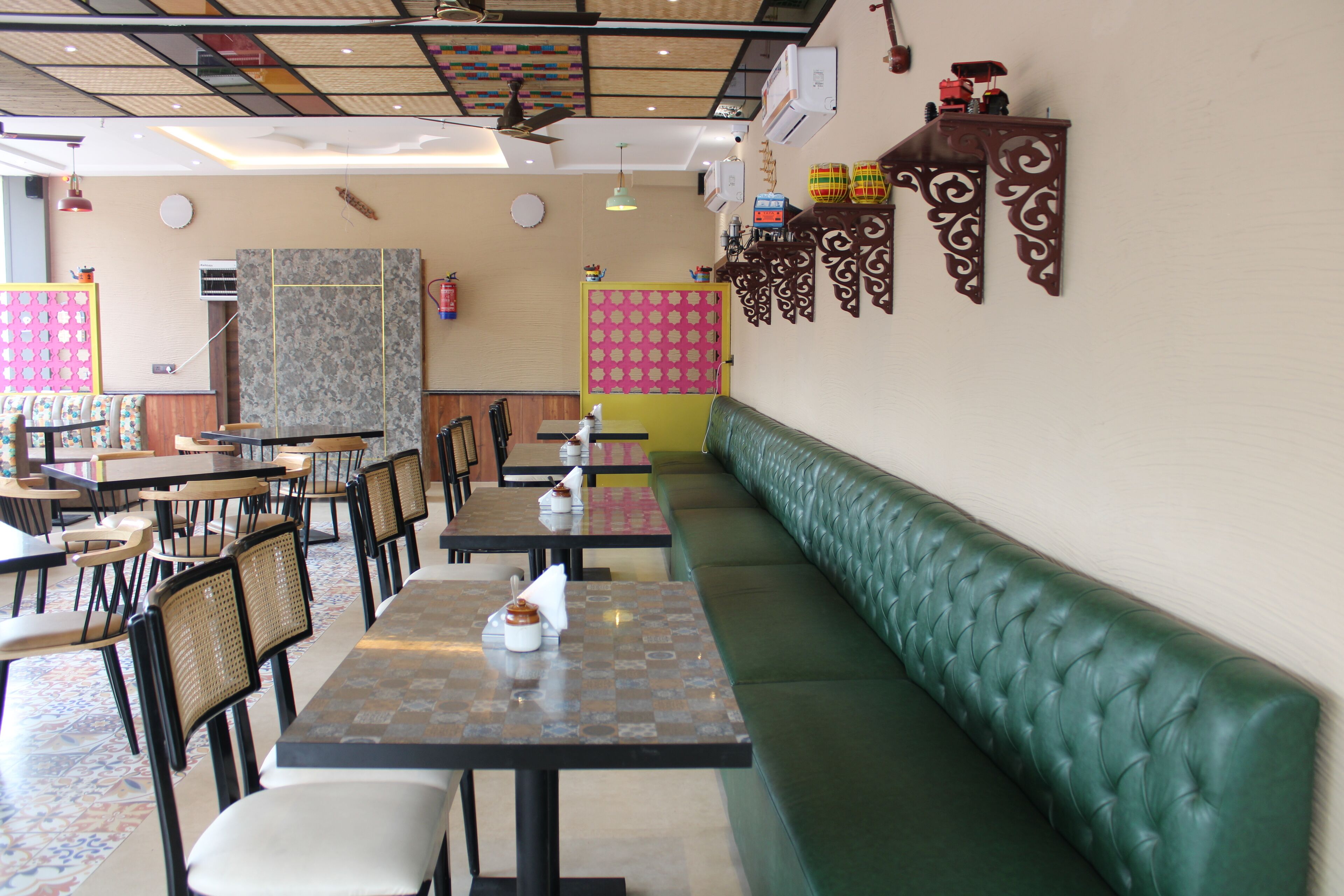 A restaurant with multiple tables and chairs, a green cushioned bench, and decorative wall panels.