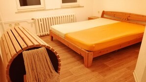 A bedroom with a wooden bed, a bench with a woven seat, and a radiator.