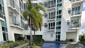 A modern building with a swimming pool, surrounded by palm trees and lounge chairs. - Comfy Studio UnitL OneMadison35 (Iloilo)