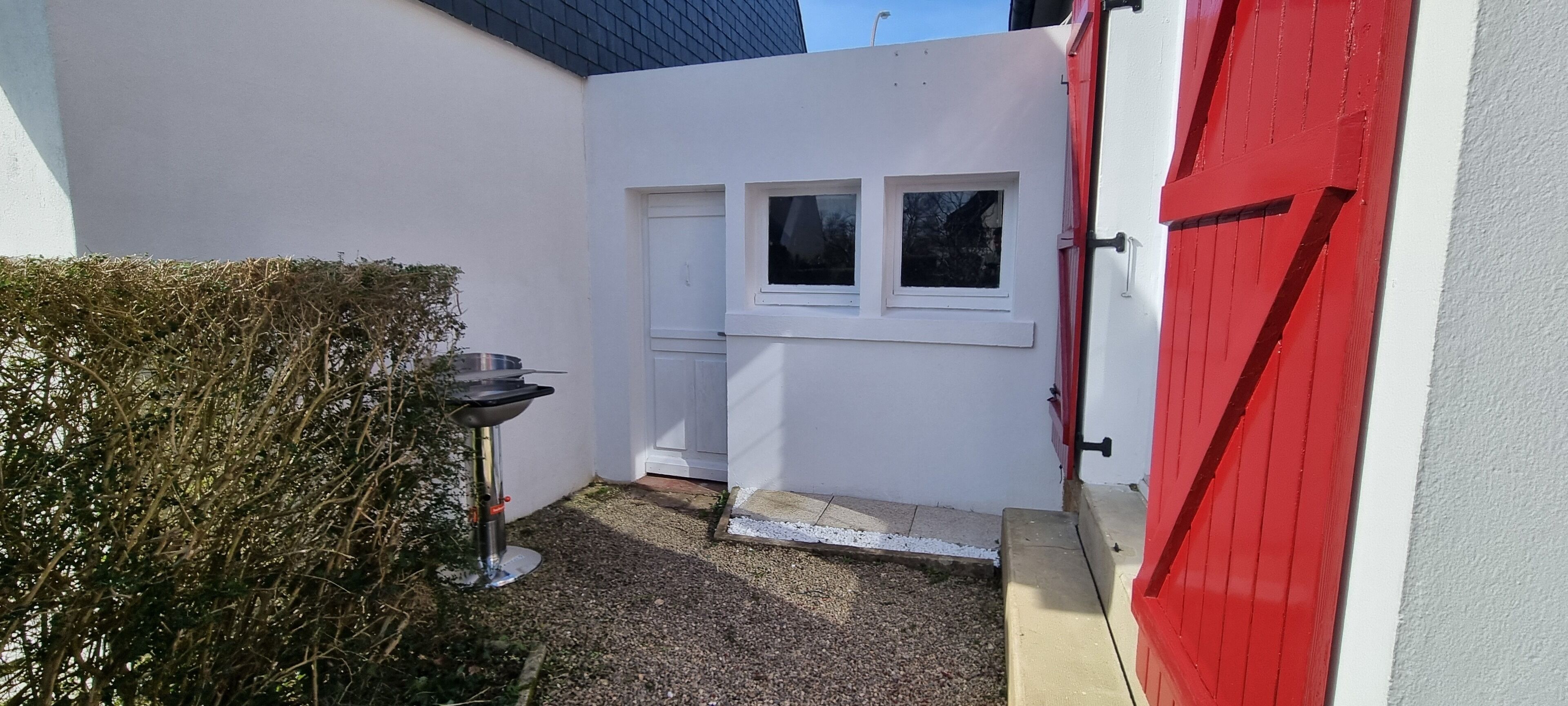A small, enclosed outdoor area with a white door and windows, a red door, and a metal table.