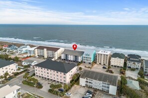 A coastal hotel with multiple buildings, a parking area, and a view of the ocean. - Windy Shores Unit 205 - Oceanfront (North Myrtle Beach)