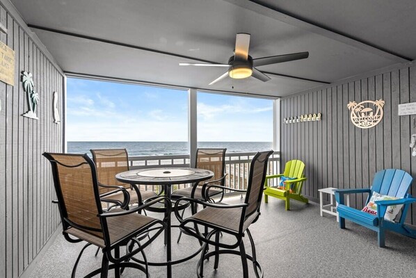 A deck with a table and chairs, a ceiling fan, and a view of the ocean. - Windy Shores Unit 205 - Oceanfront (North Myrtle Beach)