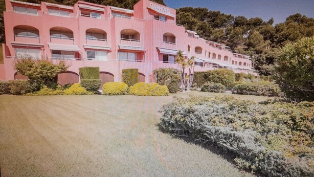Un hotel rosa con varios balcones y un jardín bien cuidado.