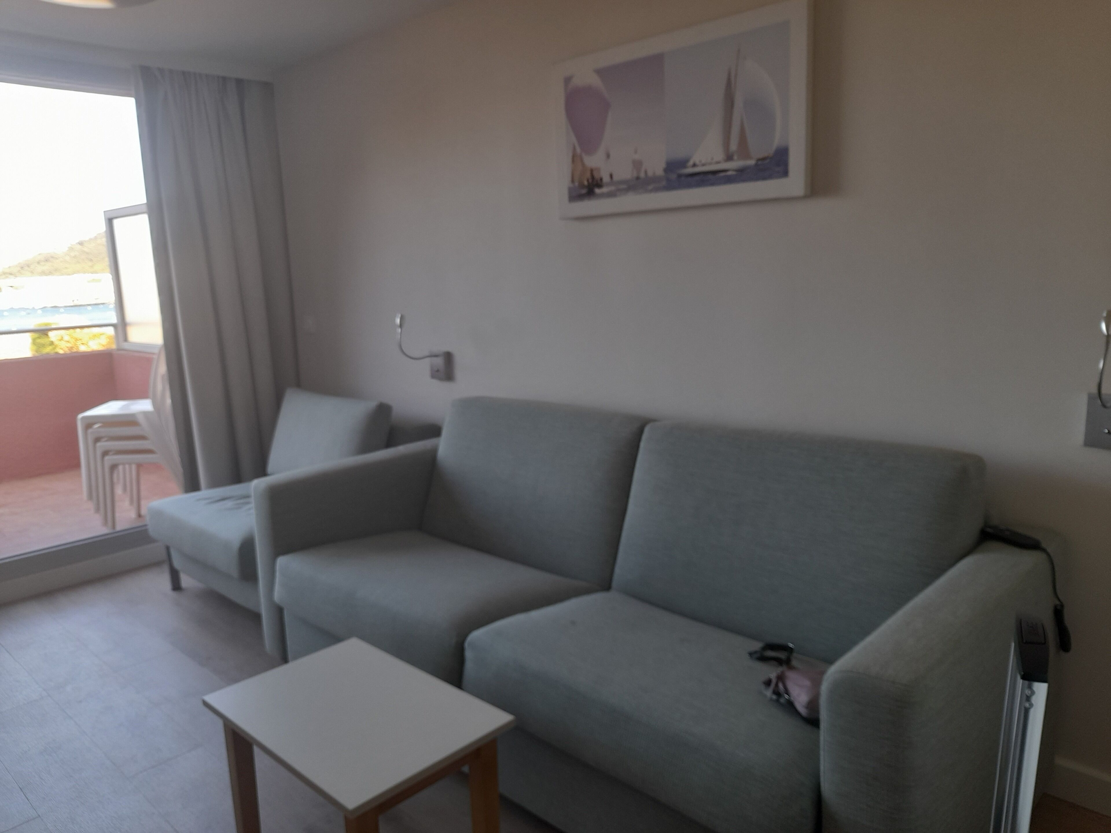 Una sala de estar moderna con un sofá gris, una mesita blanca y un cuadro de un velero en la pared.