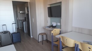 Habitación de hotel compacta con kitchenette, zona de comedor con mesa y sillas, y televisor montado en la pared.