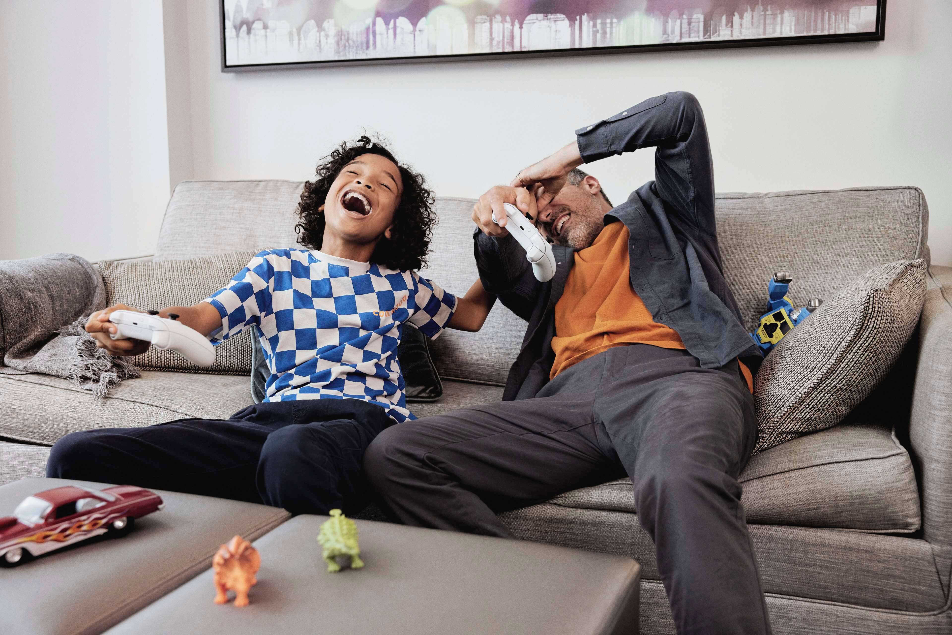 Two people sitting on a couch with a video game controller, a toy car, and a small figurine on the coffee table.