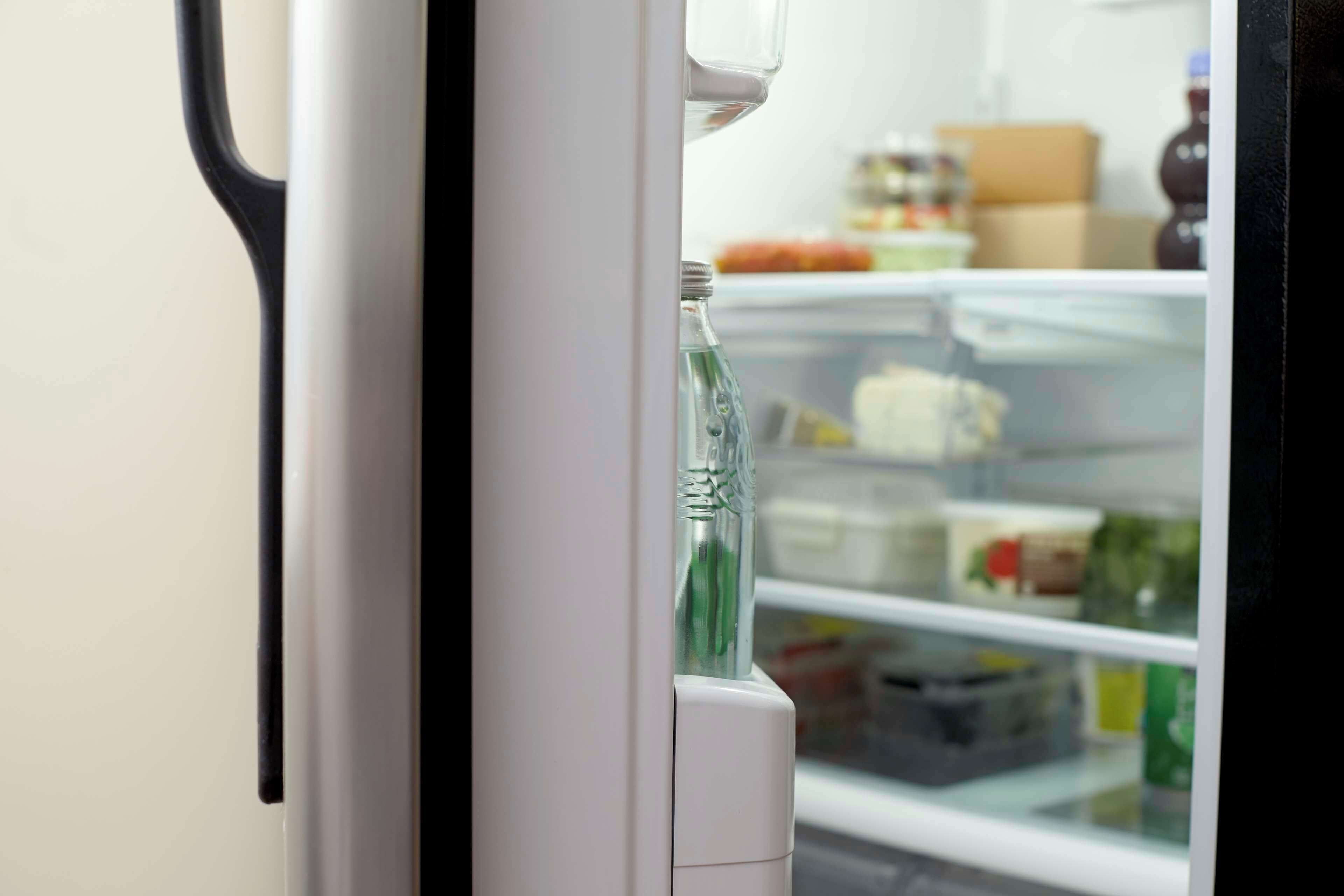 Een koelkast met waterdispenser en planken vol met verschillende soorten eten.