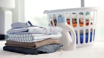 A neatly folded stack of clothing on a bed with a laundry basket in the background.