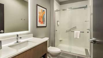 Un baño moderno con un espejo grande, un lavabo blanco, un inodoro y una ducha con mampara de vidrio.