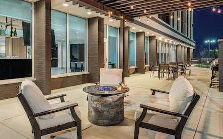 A modern outdoor patio with stone fire pit, comfortable seating, and a bar area with bottles and glasses.