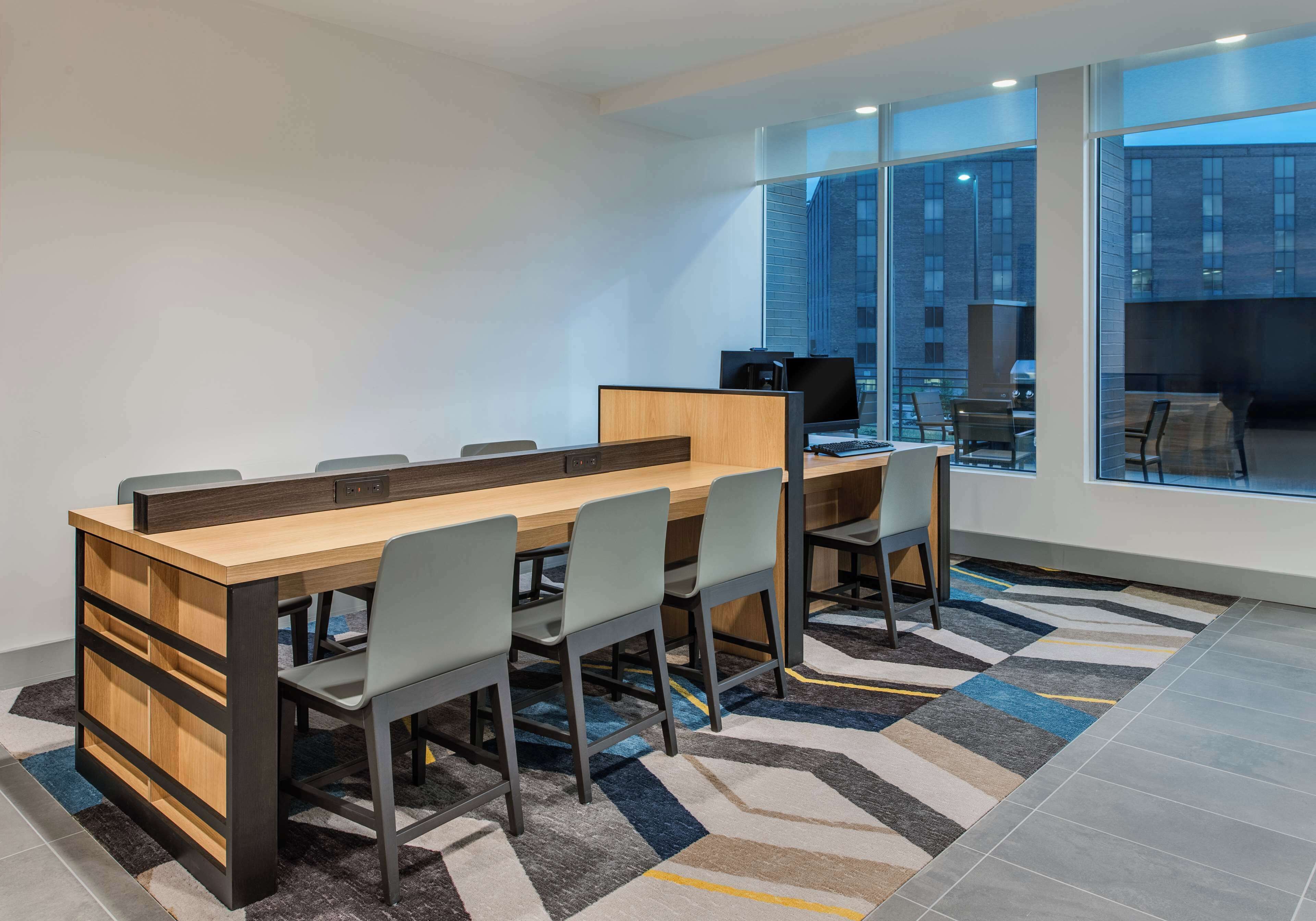 A modern conference room with a long table, six chairs, a computer, and a coffee machine.