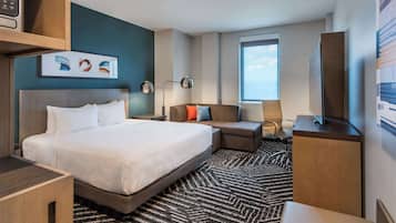 A modern hotel room with a large bed, a sofa, a desk, and a TV.