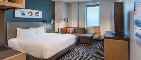A modern hotel room with a large bed, a sofa, a desk, and a TV.