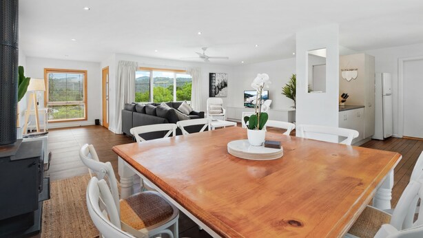A modern kitchen with white cabinets, a wooden dining table, and a view of the outdoors. - Allinga Lodge, bright, beautiful and centrally located (Jindabyne)