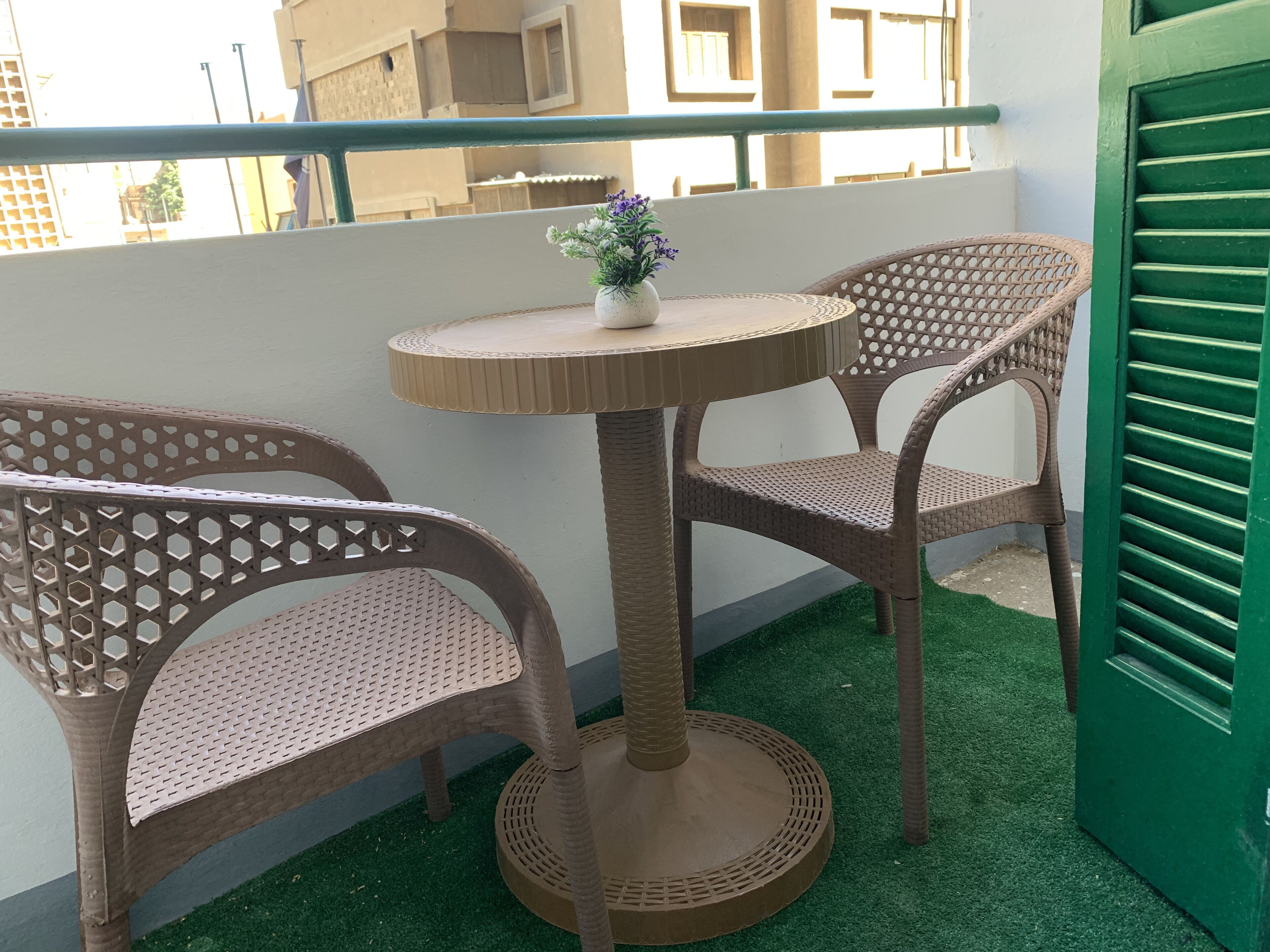 En liten sittplats utomhus med två fåtöljer i rotting och ett runt bord, en krukväxt och en grön dörr.