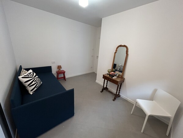 A room with a blue sofa, a white chair, a small wooden table with a mirror, and a red stool.