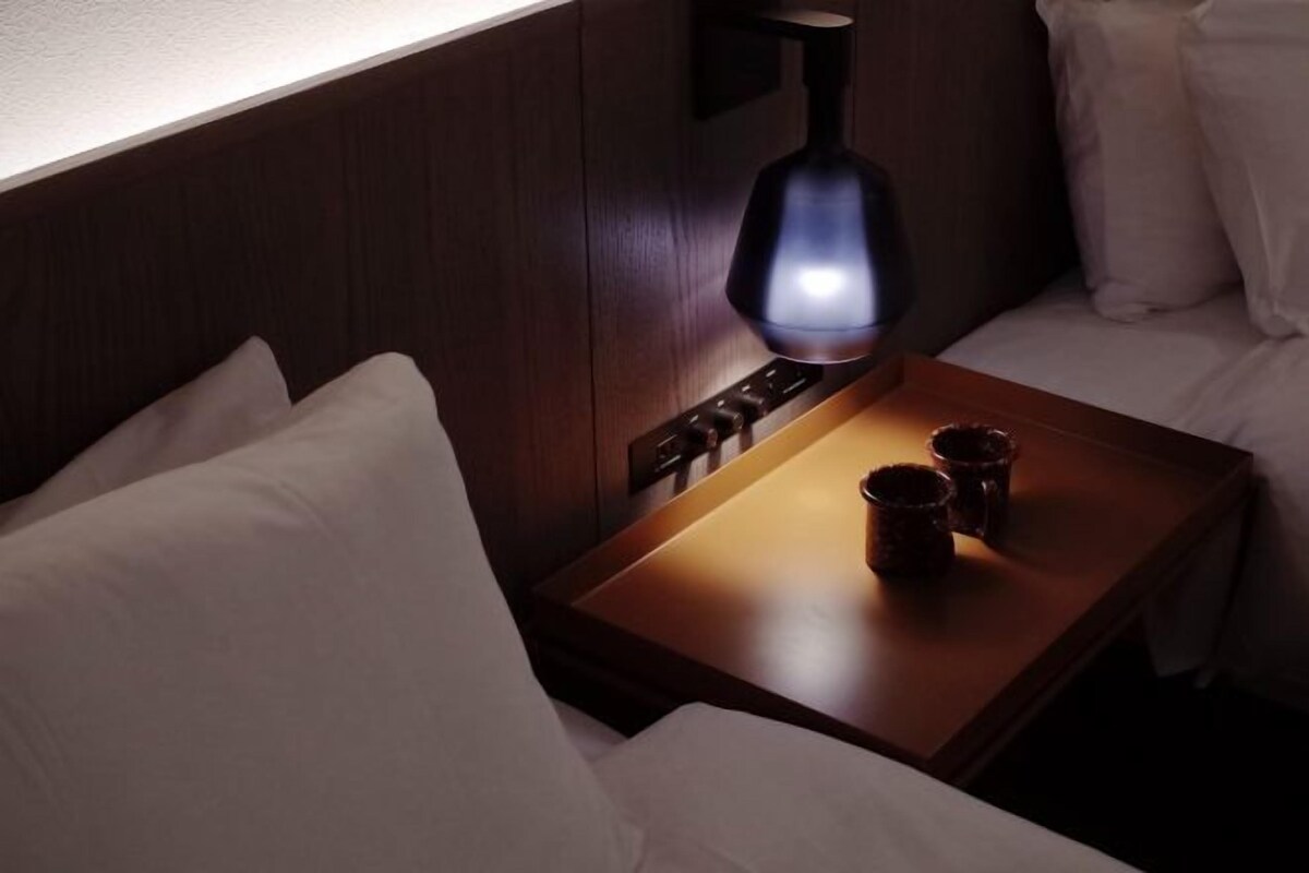 A neatly made bed with white pillows and a bedside table with a lamp and two cups.