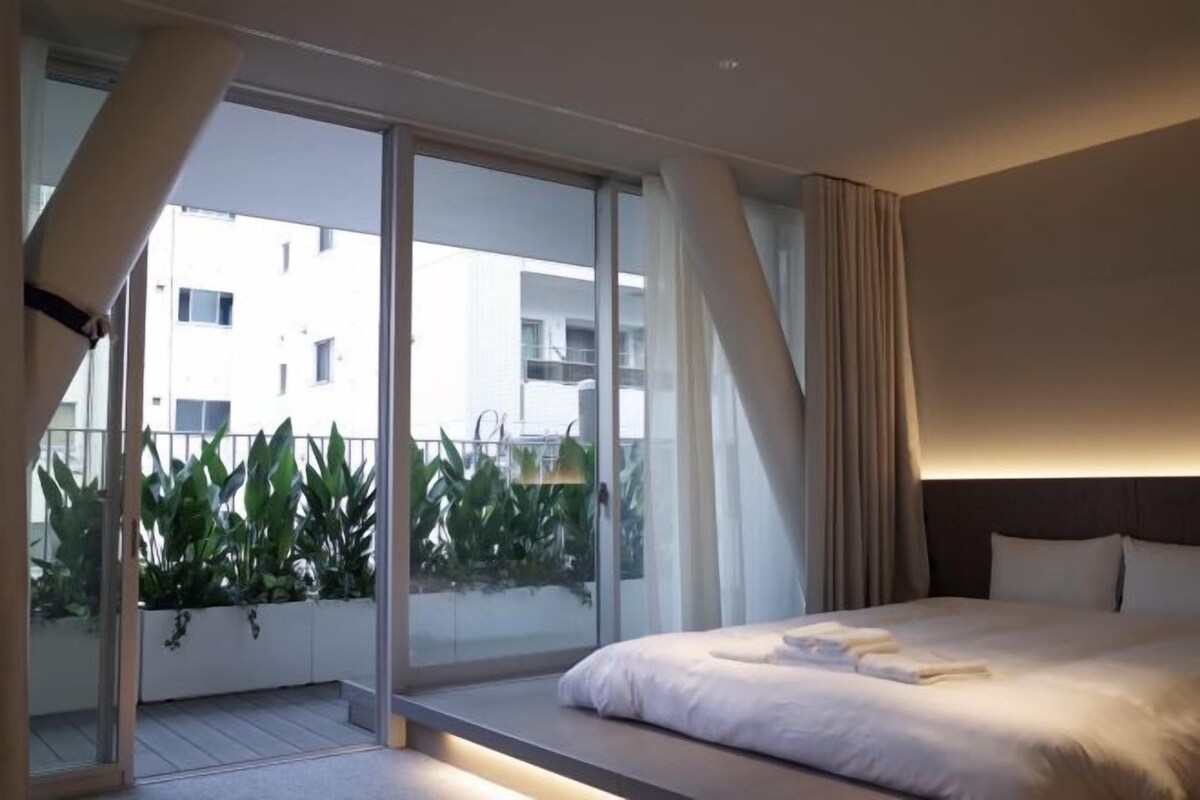 A modern hotel room with a large bed, a sliding glass door to a balcony, and a view of the cityscape.