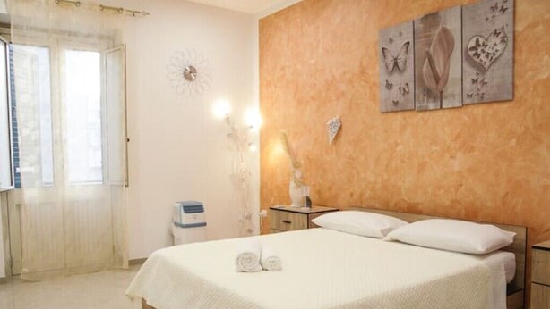 A hotel room with a bed, a nightstand, a wall clock, and a window with curtains. - 2 Bedroom Apartment in Cutrofiano (Cutrofiano)