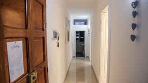 A hallway with a wooden door on the left, a white wall with a heart-shaped decoration, and a view into a room at the end. - 2 Bedroom Apartment in Cutrofiano (Cutrofiano)