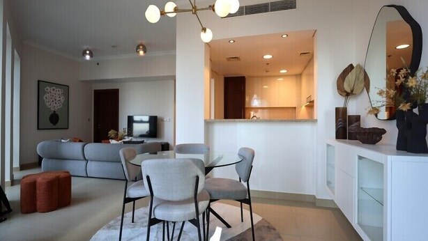 A modern living room with a sofa, a dining table with chairs, a TV, and a kitchen area with cabinets and a mirror.