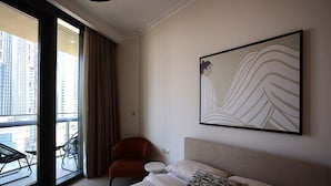 A hotel room with a bed, a chair, a round table, and a large window with a view of buildings.