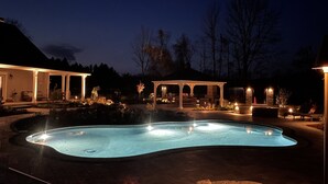 A swimming pool with a curved edge, surrounded by a patio area with seating and a gazebo. - Mountain Blossom Retreat by Evergreen Home (Lanesborough)