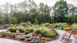 A landscaped garden with various plants and a wooden rocking chair. - Mountain Blossom Retreat by Evergreen Home (Lanesborough)