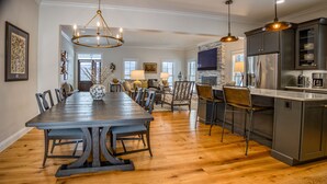 A spacious dining area with a long wooden table and chairs, a kitchen with stainless steel appliances, and a fireplace. - Mountain Blossom Retreat by Evergreen Home (Lanesborough)