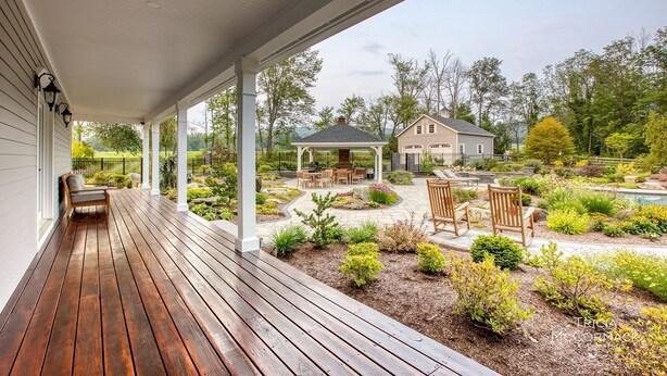 A wooden deck with a covered porch, a barbecue area, and a landscaped garden with various plants and a small pond. - Mountain Blossom Retreat by Evergreen Home (Lanesborough)