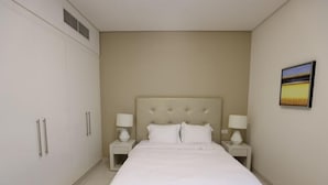 A bedroom with a large bed, two bedside tables with lamps, a wardrobe, and a painting on the wall. - Cozy 1BR Buisness bay Damac Cour Jardin (Dubai)
