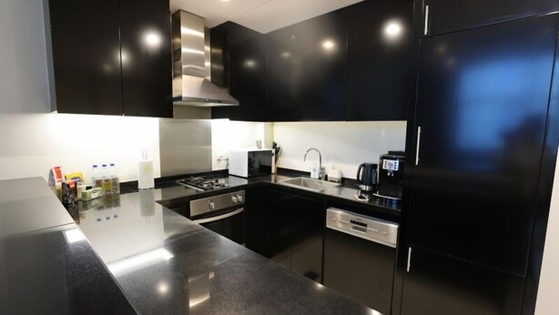 A modern kitchen with black cabinets, stainless steel appliances, and a sleek countertop. - Cozy 1BR Buisness bay Damac Cour Jardin (Dubai)