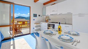 A modern kitchen with white cabinets, a dining area with blue and white plates, and a view of mountains through a glass door. - Apartment Bellavista Viddalba (Sardegna)